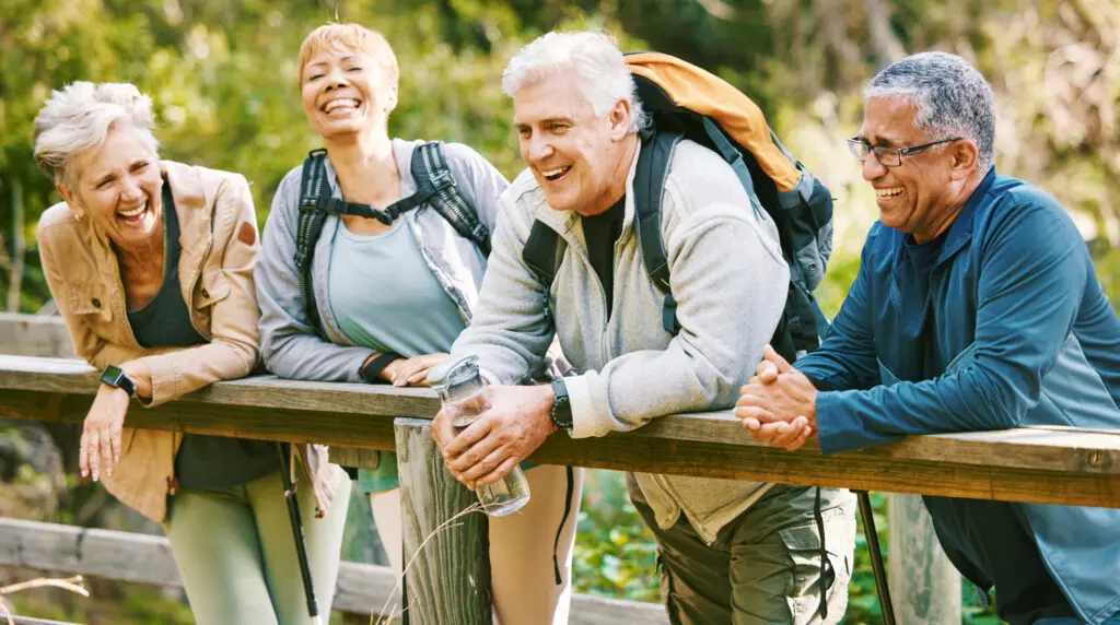 A group of seniors discovering the best clubs clubs for seniors while hiking outdoors. They are resting on a wooden bared rail.