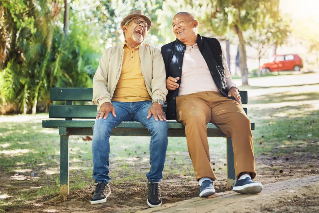 Two senior men setting on a bench discovering the best clubs for seniors. They are laughing and and enjoying senior living.