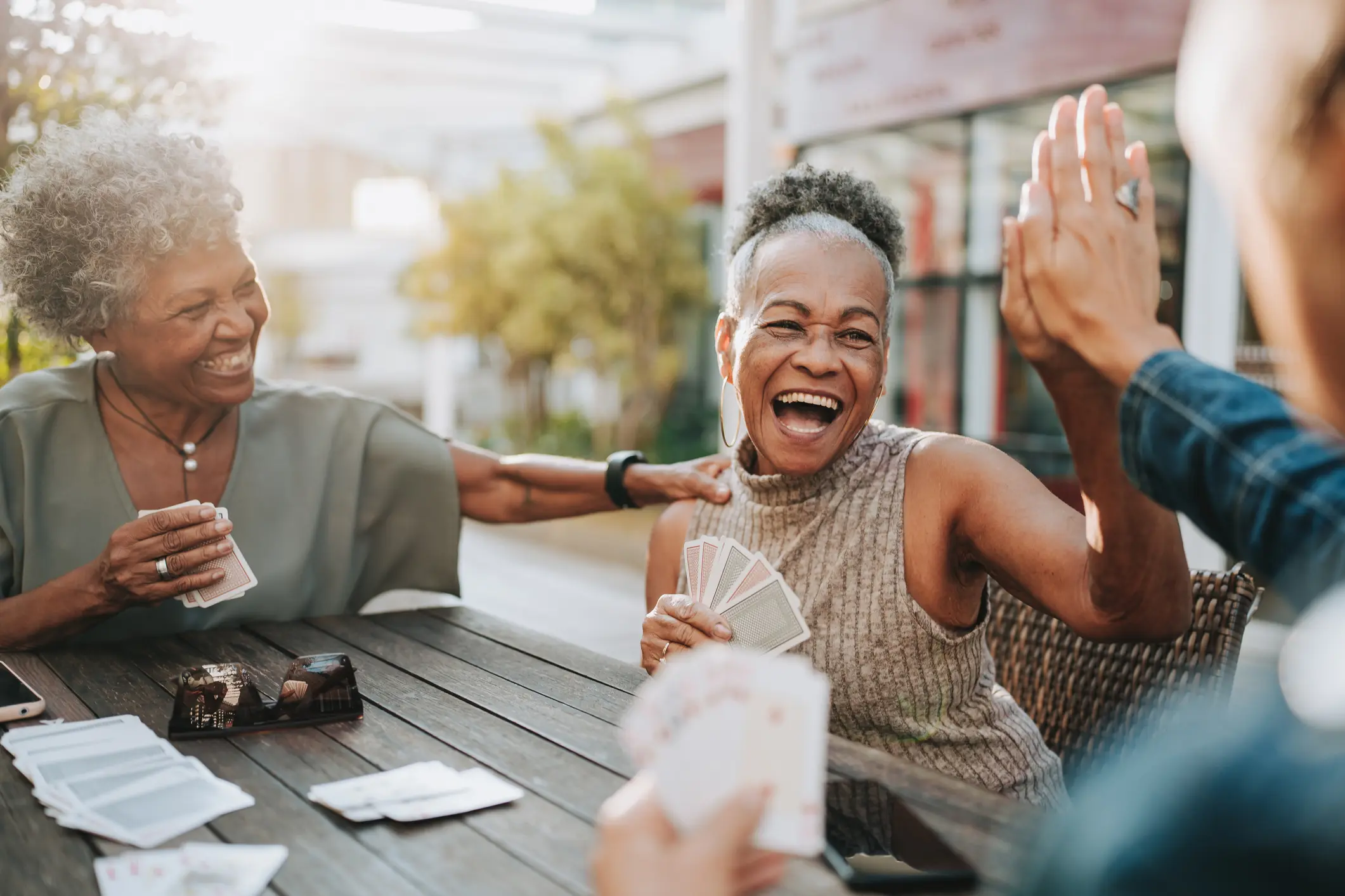 Senior woman playing cards and high fiving a friend while discovering the best clubs for seniors.