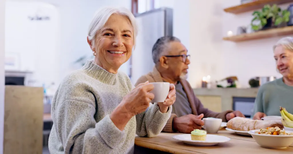 Senior woman drinking tea and smiling with friends while discussing residents' favorite services and amenities at Sedgebrook