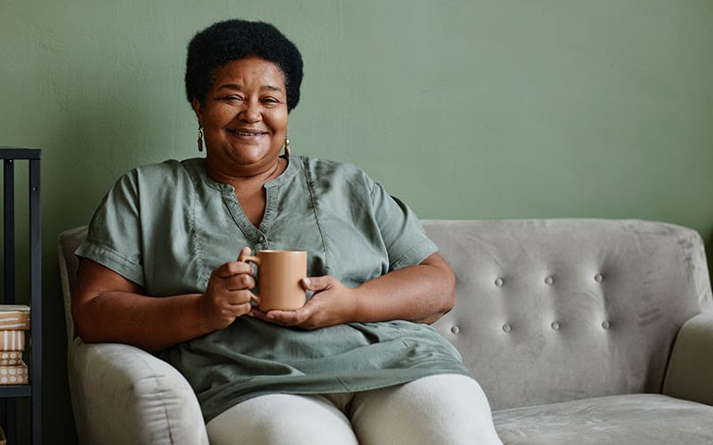 Lady sitting on a couch with a cup of coffee happy.
