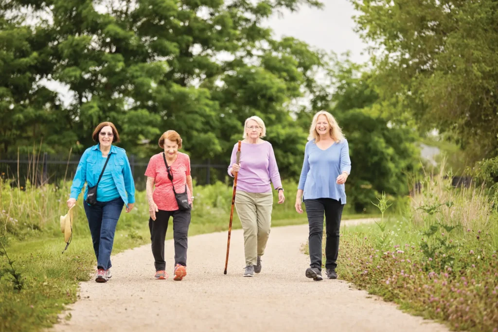 4 elderly women walking on a trail in Lincolnshire, IL to explore the health benefits of outdoor activities for seniors.